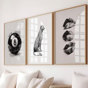 May include: Three framed wall art prints. The first features a black and white 8-ball with the text "ME". The second shows a leopard. The third print displays three lip prints. All are in wooden frames.