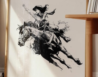 May include: Black and white framed print of a cowgirl riding a horse. The artwork depicts a dynamic scene of a woman in a hat, raising her arm while riding a bucking horse. The print is in a wooden frame.