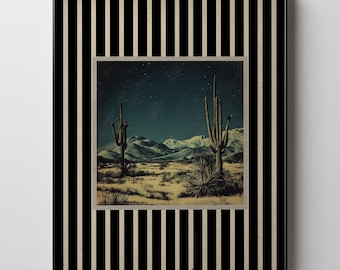 May include: A framed art print featuring a desert landscape with cacti under a starry night sky. The artwork is framed with a black and white striped border. The mountains are visible in the background.