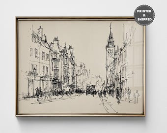 May include: A framed black and white sketch of a city street scene. The artwork depicts buildings, a clock tower, and figures, all rendered in fine lines. The frame is a gold color, and the artwork is printed and shipped.