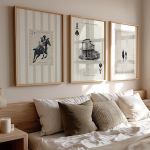 May include: Three framed art prints hang above a bed. The prints feature vintage-style imagery: a stamp with a rider on a horse, a building with an ace of spades, and a sketch of two figures. The frames are light wood, and the bed has pillows.