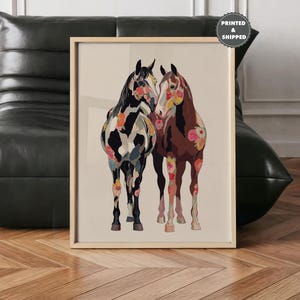 May include: A framed art print featuring two horses with floral patterns. One horse is black and white with colorful floral accents, the other is brown with pink floral details. The artwork is displayed in a light-colored wooden frame.