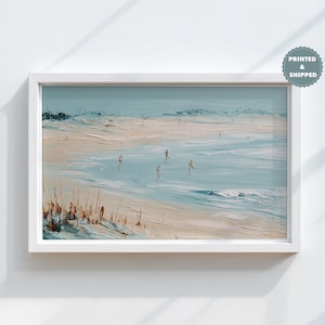 Puede incluir: Pintura enmarcada de una escena de playa con borde blanco. La obra representa una playa de arena, el océano y el cielo en tonos azules, beige y blanco. Varias figuras son visibles en el agua. La obra está etiquetada como "PRINTED & SHIPPED".