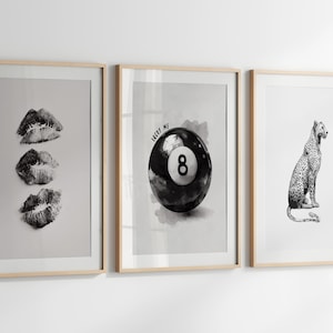 May include: Three framed black and white prints. The first features three lip prints. The second shows a black eight ball with the text "LUCKY ME". The third depicts a leopard. All are in light wood frames.