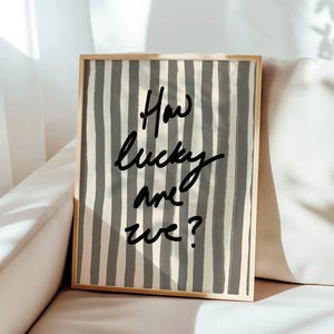 May include: A framed print with a grey and white striped background and the text "How lucky are we?" in black.