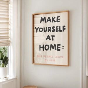 K&ouml;nnte beinhalten: Ein gerahmter Wandkunstdruck mit dem Text "MAKE YOURSELF AT HOME :) BUT PLEASE LEAVE BY 9PM" in Schwarz und Rosa. Der Druck hat einen hellen Holzrahmen und h&auml;ngt an einer wei&szlig;en Wand.
