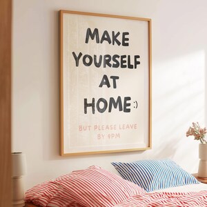K&ouml;nnte beinhalten: Ein gerahmter Wanddruck mit dem Text "MAKE YOURSELF AT HOME :) BUT PLEASE LEAVE BY 9PM" in Schwarz und Rosa. Der Druck h&auml;ngt &uuml;ber einem Bett mit rot-wei&szlig; gestreiften und blau-wei&szlig; gestreiften Kissen.