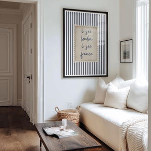May include: A framed print with a black frame and a navy blue and white striped background. The print features the text "i see london i see france" in a handwritten style. The print is hanging on a white wall.