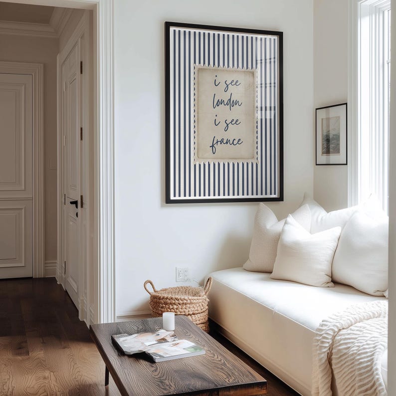 May include: A framed print with a black frame and a navy blue and white striped background. The print features the text "i see london i see france" in a handwritten style. The print is hanging on a white wall.