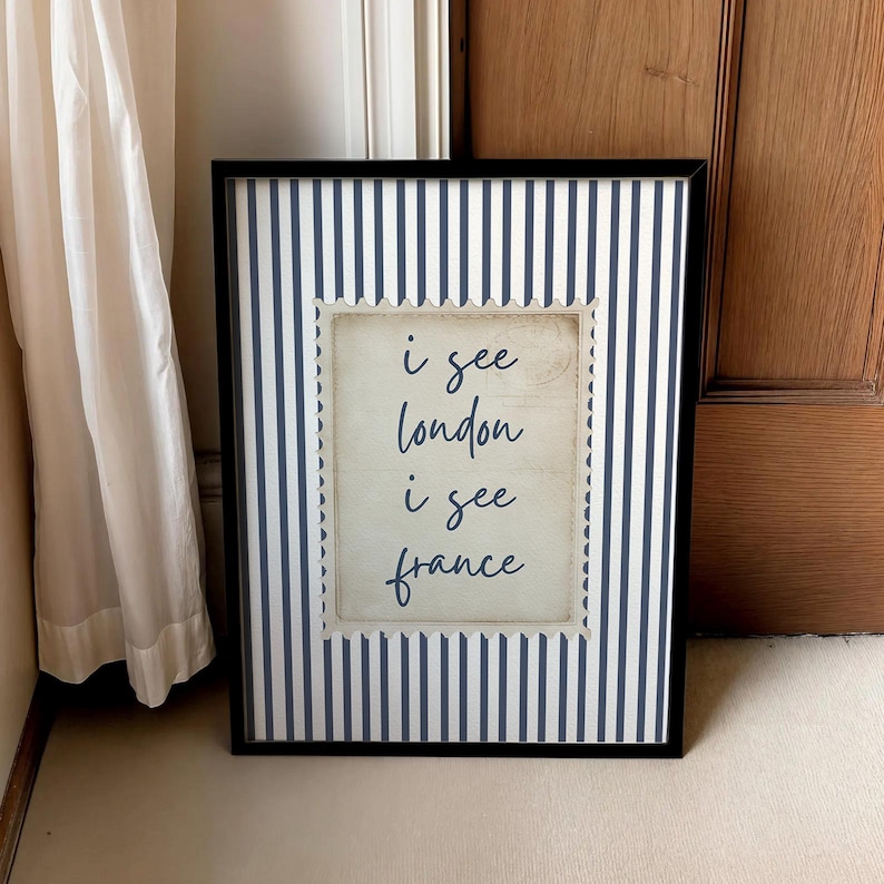 May include: Framed art print with a black border. The background features navy blue and white vertical stripes. A central, postage stamp-shaped design displays the text "i see london i see france" in a handwritten style.