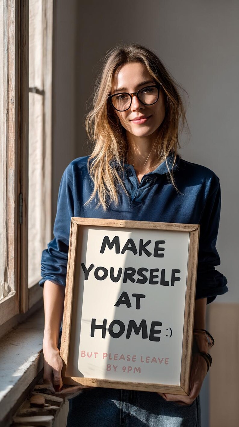 K&ouml;nnte beinhalten: Ein gerahmtes Schild mit der Aufschrift "MAKE YOURSELF AT HOME :) BUT PLEASE LEAVE BY 9PM" in schwarzer und rosa Schrift. Das Schild wird von einer Person gehalten, die ein blaues Hemd und eine Brille tr&auml;gt. Der Hintergrund umfasst ein Fenster und nat&uuml;rliches Licht.