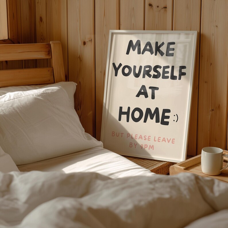 K&ouml;nnte beinhalten: Ein gerahmtes Poster mit dem Text "MAKE YOURSELF AT HOME :) BUT PLEASE LEAVE BY 9PM" steht neben einem Bett mit wei&szlig;er Bettw&auml;sche. Eine wei&szlig;e Tasse steht auf einem Holztablett.