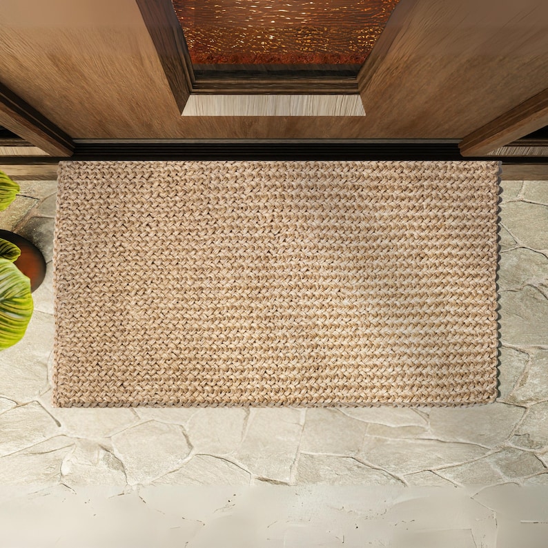 May include: A natural fiber doormat in a light brown color. The mat is made of woven strands and has a textured surface.