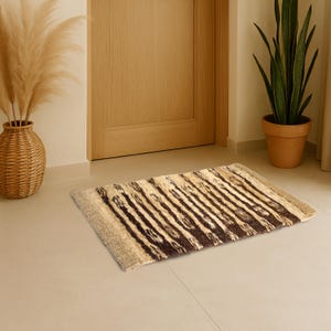 May include: A rectangular area rug featuring a repeating pattern of dark brown and cream vertical stripes. The rug has a textured, woven appearance with solid cream-colored borders on the left and right edges, lying flat on a light-colored floor.