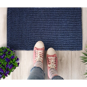 May include: A blue knitted doormat with a woven texture. A pair of pink canvas shoes with white laces are standing on the mat.