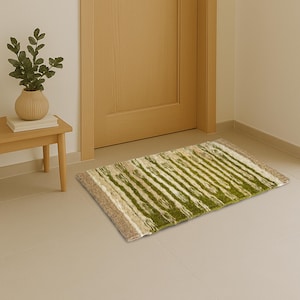 May include: A rectangular floor mat featuring a textured, shaggy pile with a repeating pattern of vertical stripes in shades of olive green, cream, and beige, finished with solid beige borders on the left and right edges of the mat.