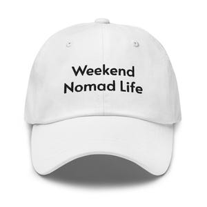 May include: A white baseball cap with the text "Weekend Nomad Life" in black. The cap has a curved brim and an adjustable strap at the back. The hat is made of a soft, durable material.