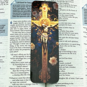 May include: A religious card featuring a depiction of Jesus Christ on the cross. The card has a blue background with white flowers and gold accents. The text on the card reads "5:18 Good for Something" and "Wisdom".
