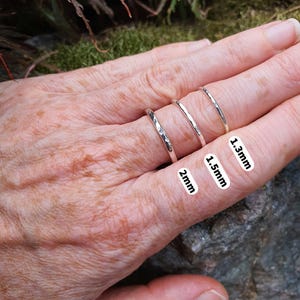 May include: Three silver rings with a hammered texture, each featuring a different band width. The rings are labelled with text indicating their specific thicknesses of 2mm, 1.5mm, and 1.3mm, providing a clear visual comparison of the three sizes.