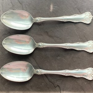 May include: Three silver spoons with ornate handles. The spoons are arranged in a row, with the handles pointing to the right.