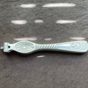 Peut inclure: Un casse-noisettes en argent avec un motif décoratif sur la poignée. Le motif représente un soleil stylisé avec un visage et un motif floral.