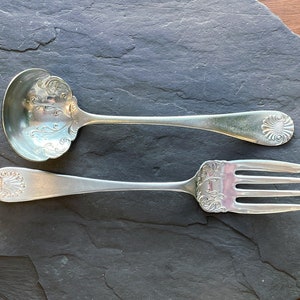 Peut inclure: Un ensemble de service en argent avec une cuillère et une fourchette décoratives. La cuillère a un bol arrondi et un long manche avec un motif orné. La fourchette a trois dents et un motif orné similaire sur le manche.