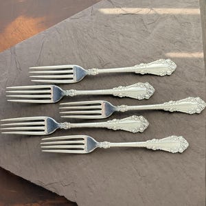 Può includere: Sei forchette d'argento con dettagli floreali ornati sui manici sono disposte su un'ardesia grigio scuro. Ogni forchetta ha tre rebbi, ideali per una cena formale. Misurano circa 20 cm di lunghezza.