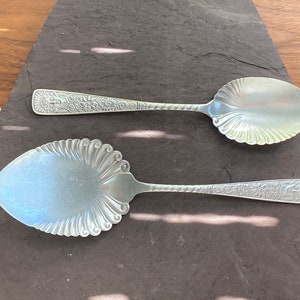 May include: Two silver serving spoons with ornate handles. The spoons have a decorative, scalloped design on the bowl.