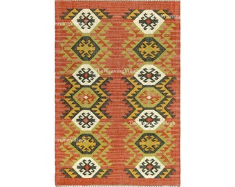 May include: A rectangular woven rug with a geometric pattern. The rug has a terracotta background with repeating diamond and zigzag patterns in yellow, black, and white. The edges have a fringed trim.