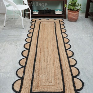 May include: A natural fiber rug with a black border and scalloped edges. The rug is made of jute and has a natural, earthy color.