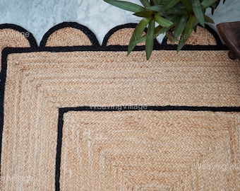 May include: A natural fiber rug with a black border and a scalloped edge. The rug has a square shape with a smaller square inside.