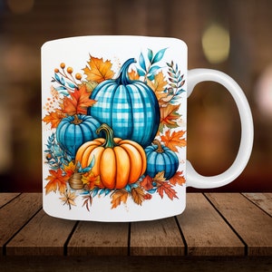 May include: White ceramic mug with a fall-themed design featuring three pumpkins. The pumpkins are blue and orange with a plaid pattern. The design also includes fall leaves and berries.