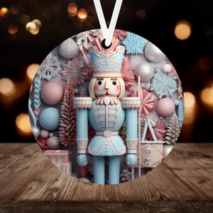 May include: A round Christmas ornament featuring a light blue and pink nutcracker soldier. The ornament has a white ribbon for hanging and is decorated with pastel-colored holiday elements, including snowflakes and ornaments. The background is blurred with warm bokeh lights.