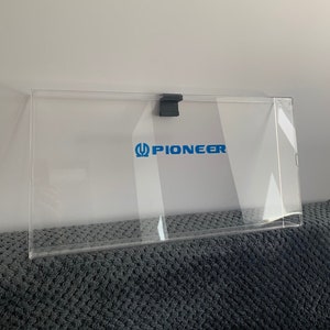 Könnte beinhalten: Eine transparente Acryl-Vitrine mit einem schwarzen Clip oben. Die Vitrine trägt den Schriftzug "PIONEER" in Blau auf der Vorderseite.