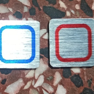 Pode incluir: Seis etiquetas quadradas de metal com borda preta e fundo branco. As etiquetas têm bordas de cores diferentes: prata, cinza, cinza claro, azul e vermelho.