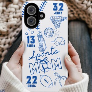 May include: White phone case with blue sports-themed illustrations, including a baseball, basketball net, golf bag, volleyball, and football. The words "Sports Mom" are featured, along with the names and numbers "32 Jenny", "13 Randy", and "22 Chris".