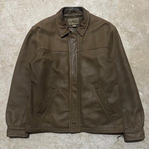May include: A brown leather jacket with a collared neckline and two front pockets. The jacket has a button closure and a label that reads "Rainforest". The jacket is a medium size.