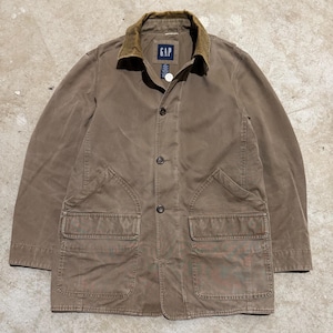 May include: A brown GAP jacket with a corduroy collar and button-up front. The jacket has two large front pockets and a small GAP label on the chest. The jacket is a neutral color and appears to be made of a durable material.