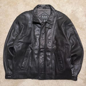 May include: A black leather jacket with a collared neckline and a button-up front. The jacket has two front pockets and a label that reads "RBM". The jacket is a classic style.