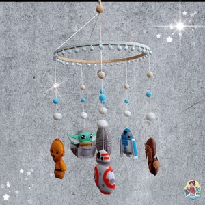 Pode incluir: Móbile para bebé com tema Star Wars, com personagens de feltro como Baby Yoda, R2-D2 e Chewbacca. O móbile tem um aro de madeira com detalhes azuis e brancos, e bolas de feltro penduradas em vários tamanhos e cores. Os personagens estão suspensos no aro.