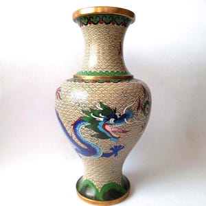 Peut inclure: Un vase décoratif avec un fond beige et un motif de dragon coloré. Le vase a un bord et une base dorés, avec des accents verts et bleus. Le dragon est bleu et vert avec une bouche rouge.