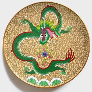 Pode incluir: Prato decorativo redondo com um design de dragão verde e detalhes vermelhos sobre um fundo dourado com um padrão de nuvens. O prato tem uma borda dourada e é um item decorativo.