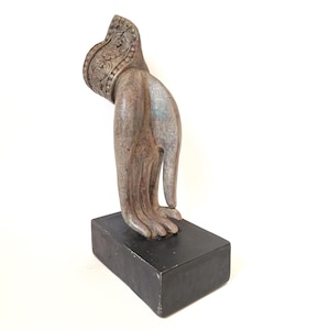 Può includere: Scultura di una mano in stile antico, montata su una base rettangolare nera. La mano è dettagliata con intagli intricati e presenta una finitura sbiadita e multicolore. La scultura sembra essere realizzata in materiale composito.