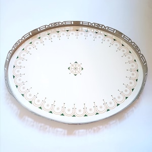 May include: Oval serving tray with a white interior and a decorative border. The tray features a silver-colored metal rim with a geometric design. The interior has a repeating pattern of green and gold accents, with a central geometric design.