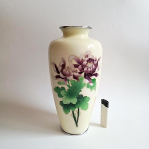 Pode incluir: Um vaso de cor creme com borda prateada apresentando um design pintado de flores de crisântemo roxas e folhas verdes. Um isqueiro branco está posicionado ao lado do vaso para escala, mostrando que o vaso tem cerca de 20 cm de altura.