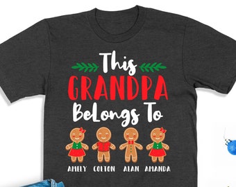 May include: A dark gray t-shirt with the text "This Grandpa Belongs To" in white and red. Below the text are four gingerbread people with the names "Amely, Colton, Alan, Amanda" written underneath.