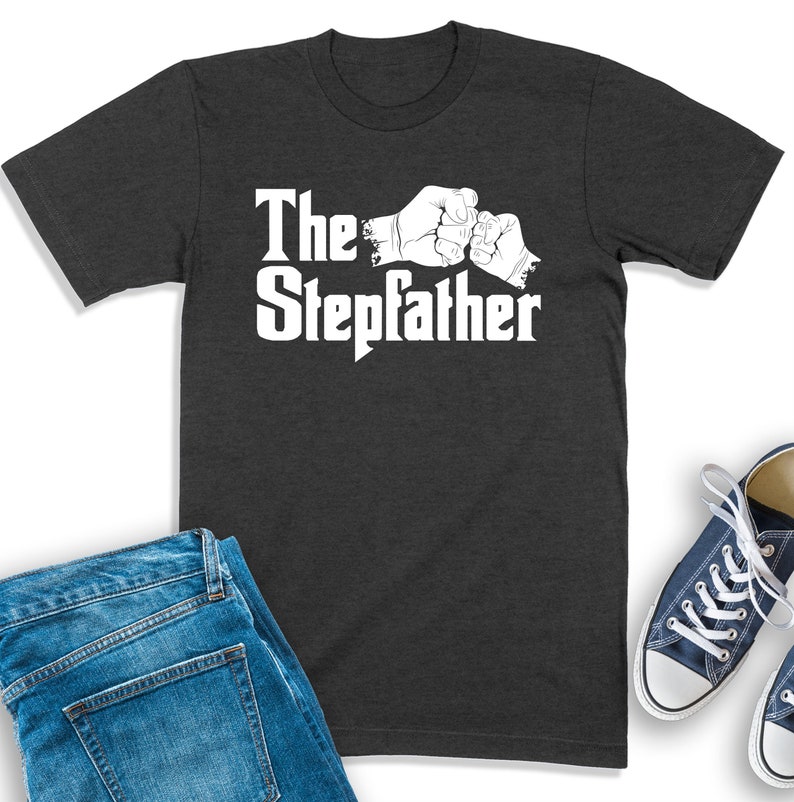 K&ouml;nnte beinhalten: Ein dunkelgraues T-Shirt mit einer wei&szlig;en Grafik von zwei H&auml;nden, die sich die F&auml;uste sto&szlig;en, und dem Text "The Stepdad" auf der Vorderseite.
