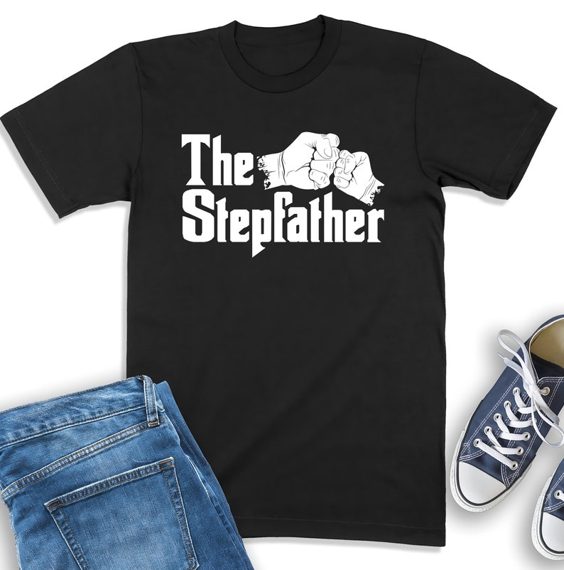 K&ouml;nnte beinhalten: Schwarzes T-Shirt mit wei&szlig;em Text "The Stepdad" und einer Grafik von zwei sich sto&szlig;enden F&auml;usten.