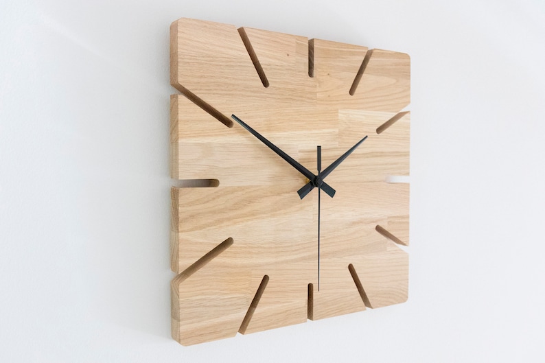 Pu&ograve; includere: Un orologio da parete quadrato in legno con lancette nere e un design unico con tagli attorno ai bordi.