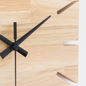 Pu&ograve; includere: Primo piano di un quadrante di orologio in legno con lancette delle ore e dei minuti nere. Il quadrante dell'orologio &egrave; in legno chiaro con una venatura naturale.